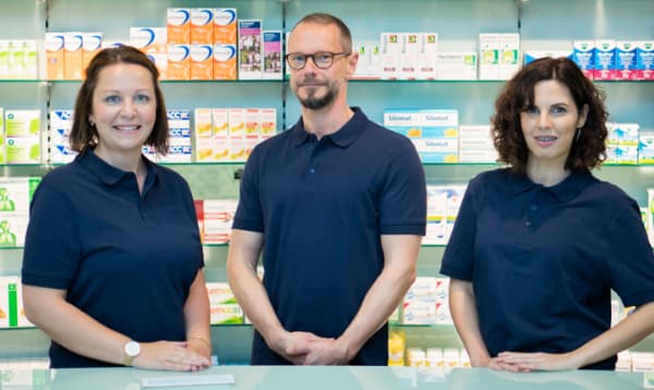 Drei Mitarbeitende von Axels Apotheke vor dem Arzneimittelregal